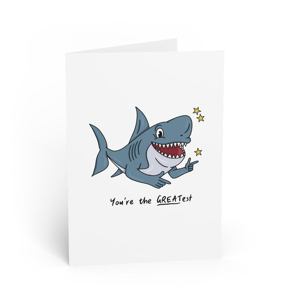 Greeting card of a cartoon shark with arms and hands doing finger guns with the below text saying "you're the greatest"